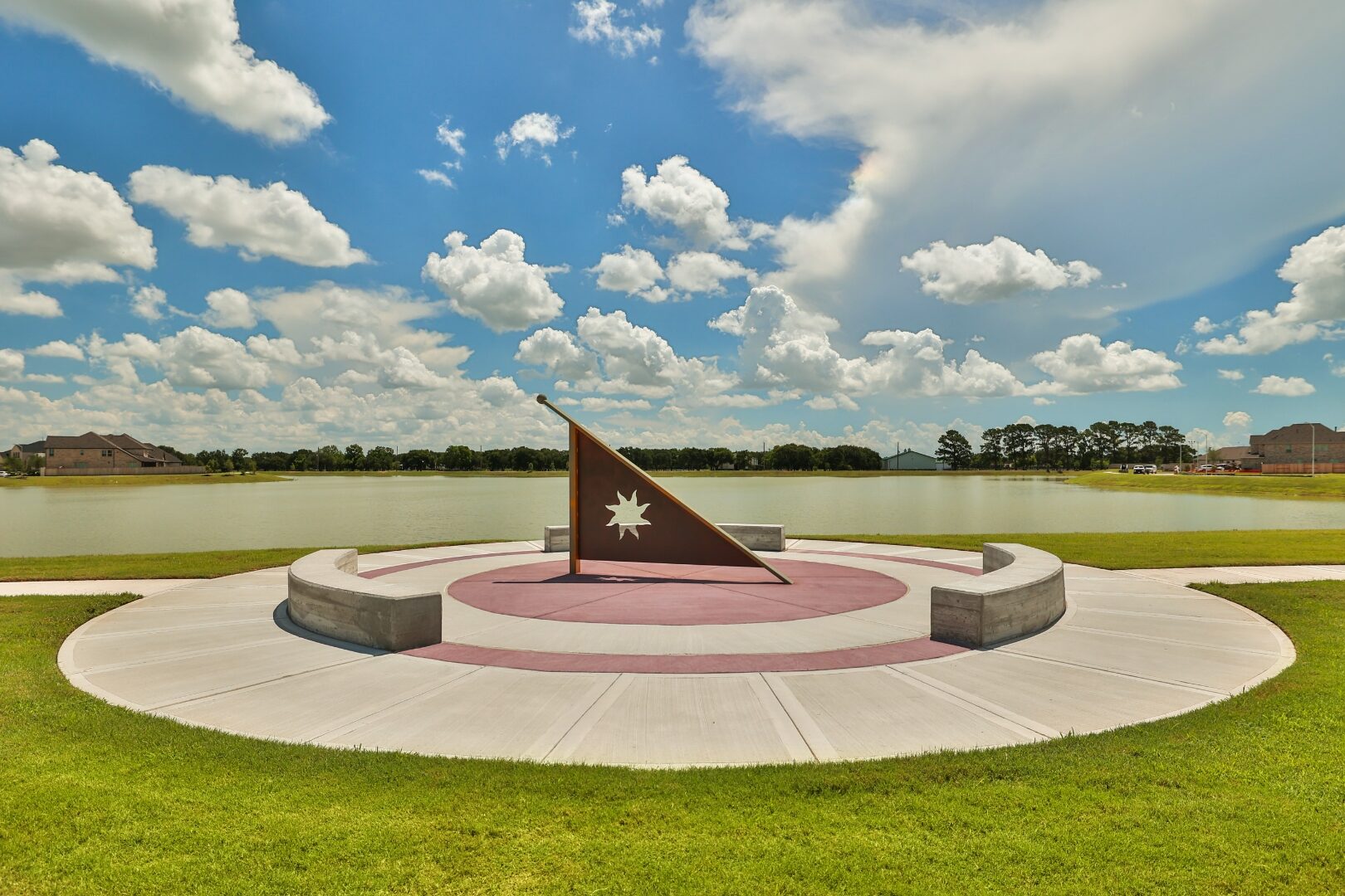 Corten steel sundial on a radial concrete plaza beside a lake